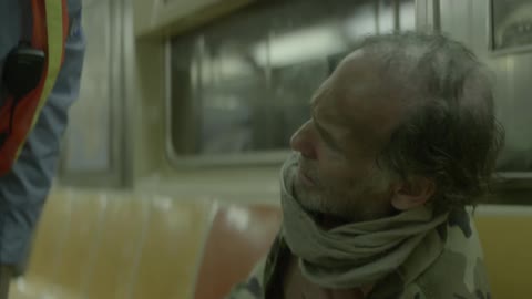 A worker shakes a homeless man awake on a train
