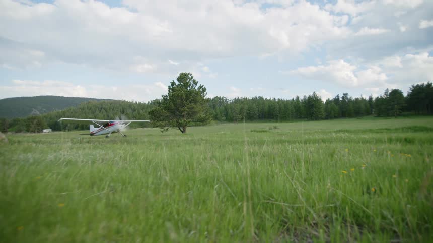 Single engine airplane moving across a grass field with trees around during daytime