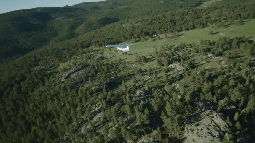 Small private plane flying over mountains with forests
