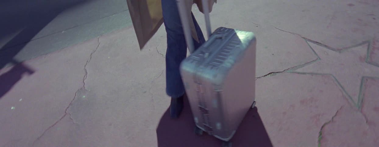Woman rolls a suitcase over stars on the sidewalk