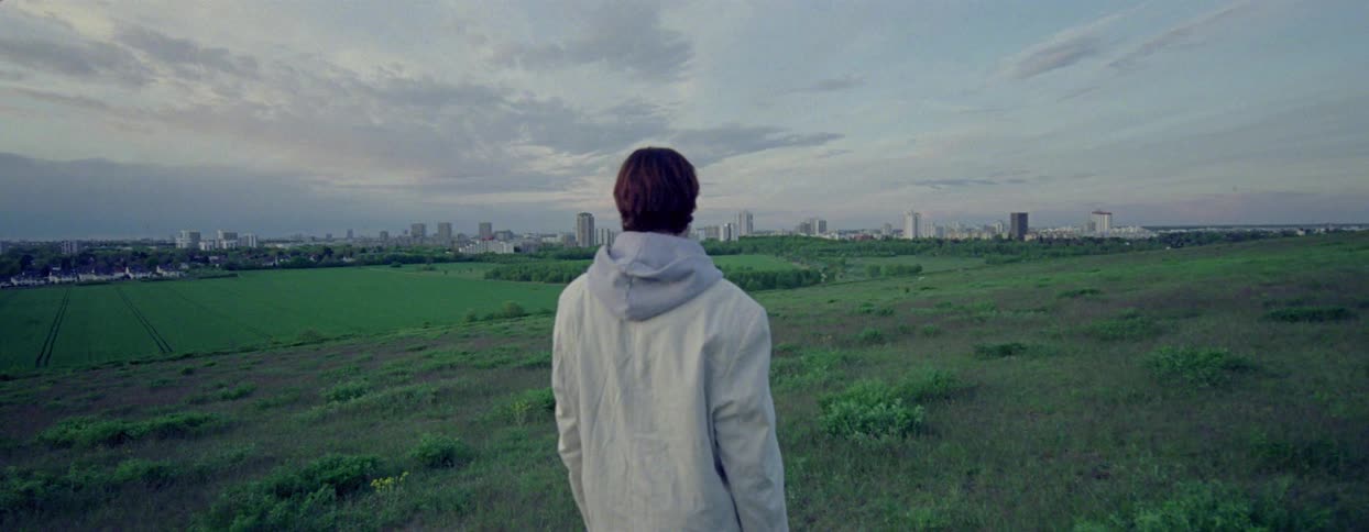A person stands on a grassy slope and looks out at the metropolis in the distance