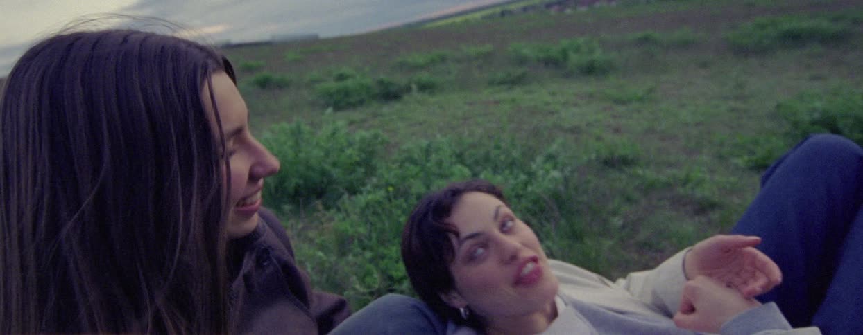 Two happy friends sitting in a field talking