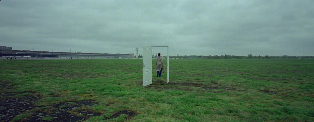Person walking through an open gate in the middle of a field on a cloudy day