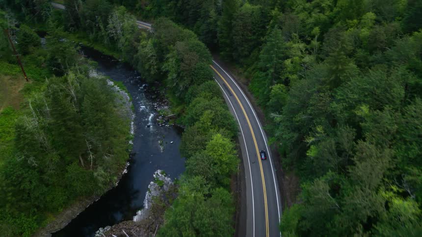 Aerial view of a car traveling along a highway surrounded by vegetation and next to a river