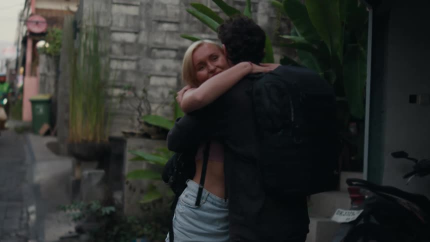 Woman hugs man before walking away along narrow road filled with motorcycles
