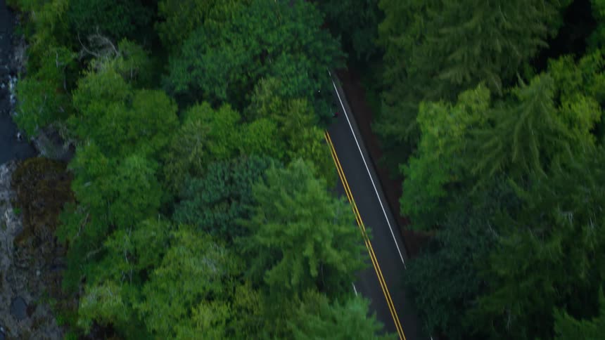 Aerial view of a black vehicle traveling on a highway surrounded by trees and next to a river