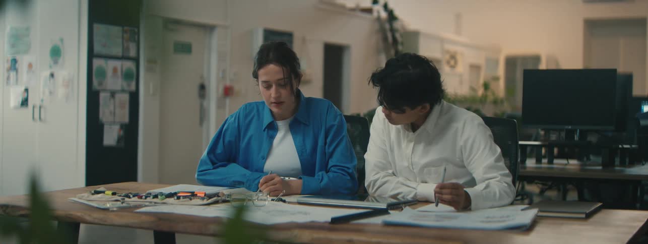 Woman with robotic arm sitting next to a man at a table with books