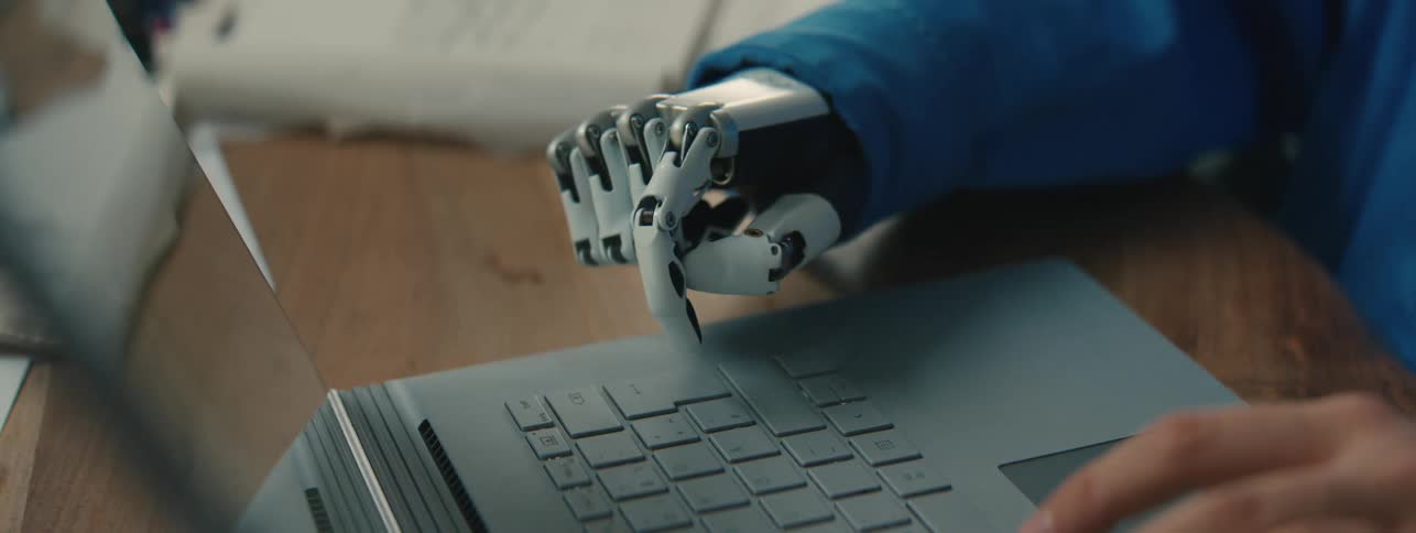 A woman with a prosthetic hand types on a laptop