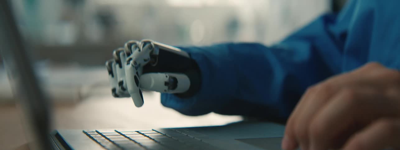 Human and robotic hand typing on a laptop
