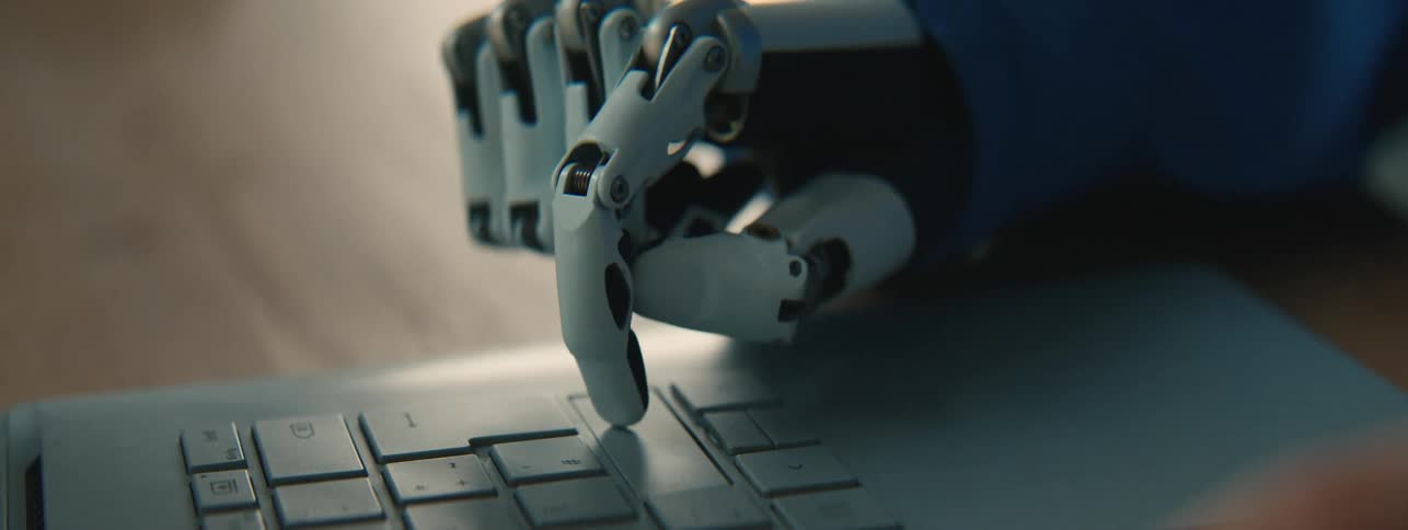 A robotic prosthesis hand with metal components presses keys on a laptop keyboard