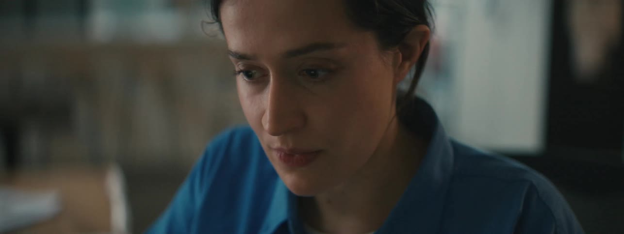 A contemplative worried woman leaning back on her chair as she rubs the side of her forehead then leans forward and frowns
