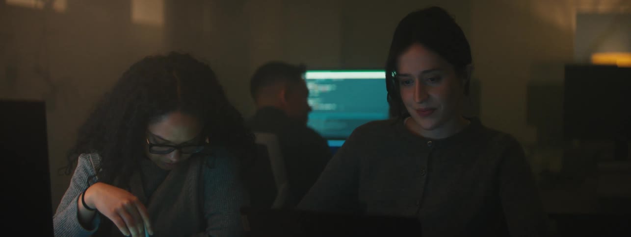 A man and three women sit in a dark computer lab