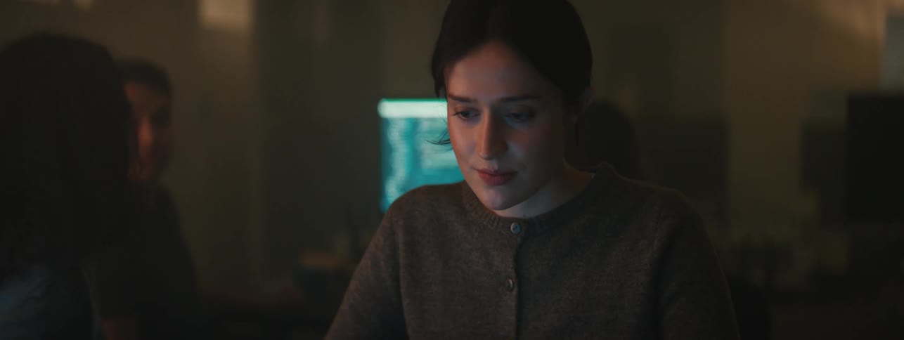 Close up of the face of a woman wearing a sweater working on a dimly lit room