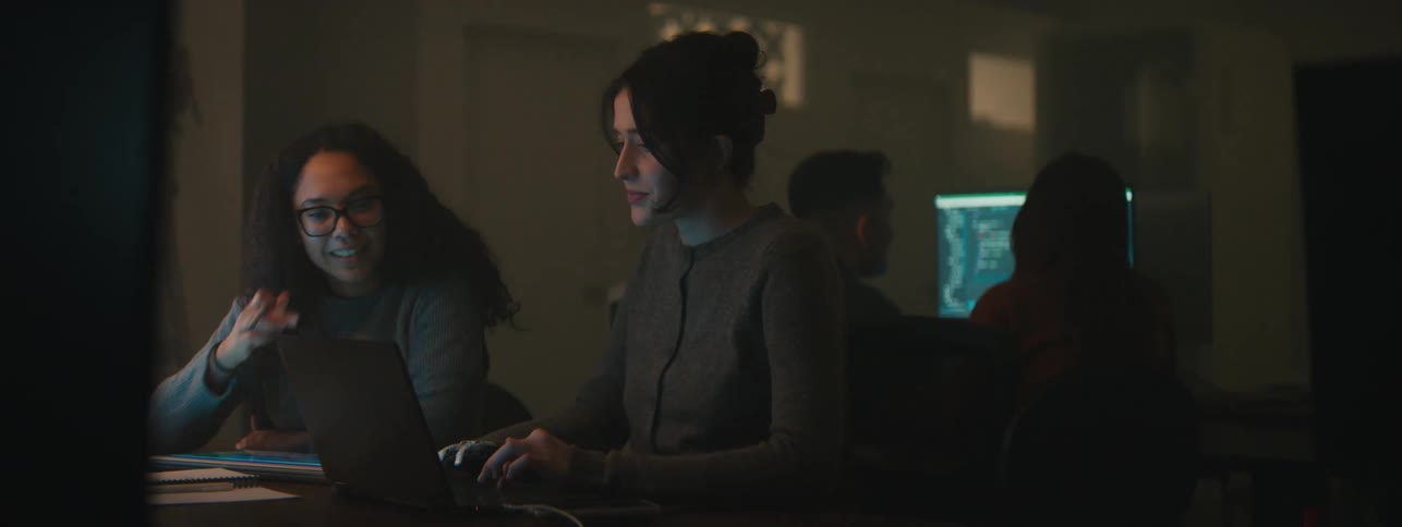 Women sitting at a table collaborate using a laptop