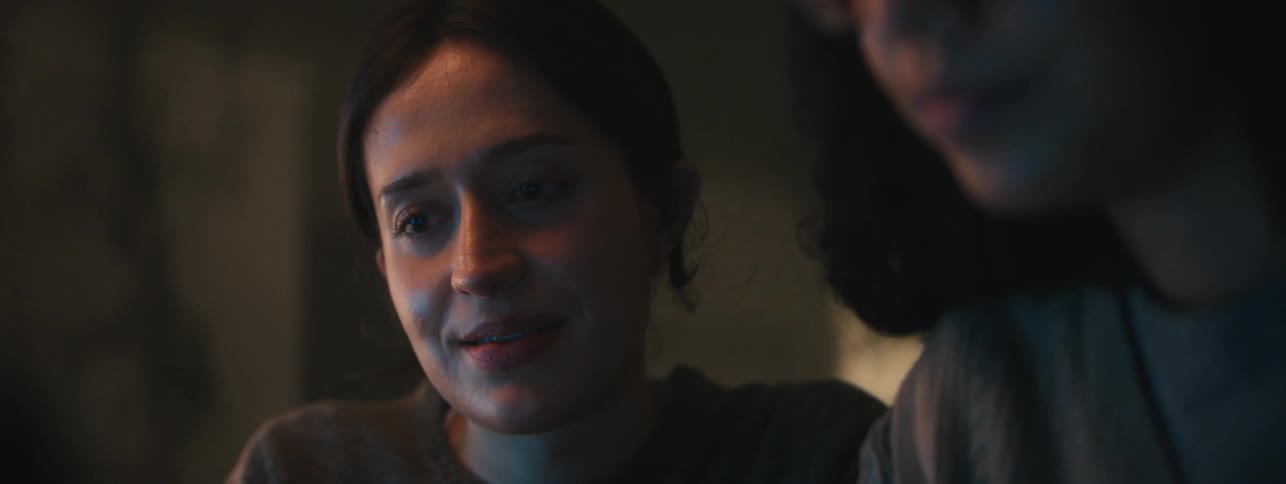 Computer light shines on two women collaborating in a dimly lit room