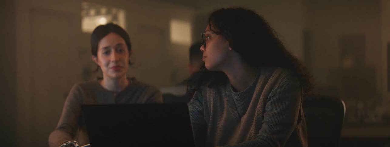 Two women talk while using a laptop
