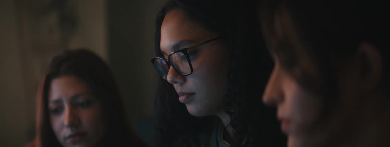 Three women side by side talking nodding and smiling while staring at a computer the light from which shines on their faces