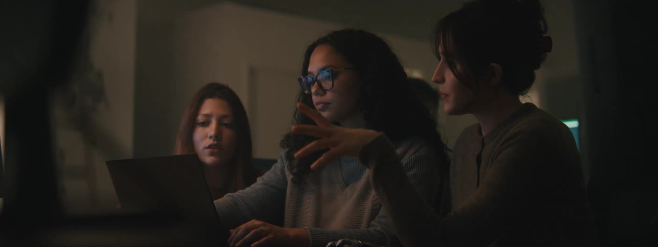 Three women talk and point at a laptop