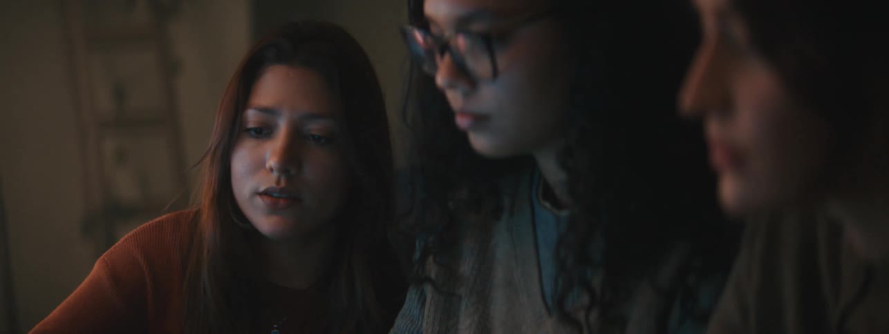 Three women talk together while looking at a display