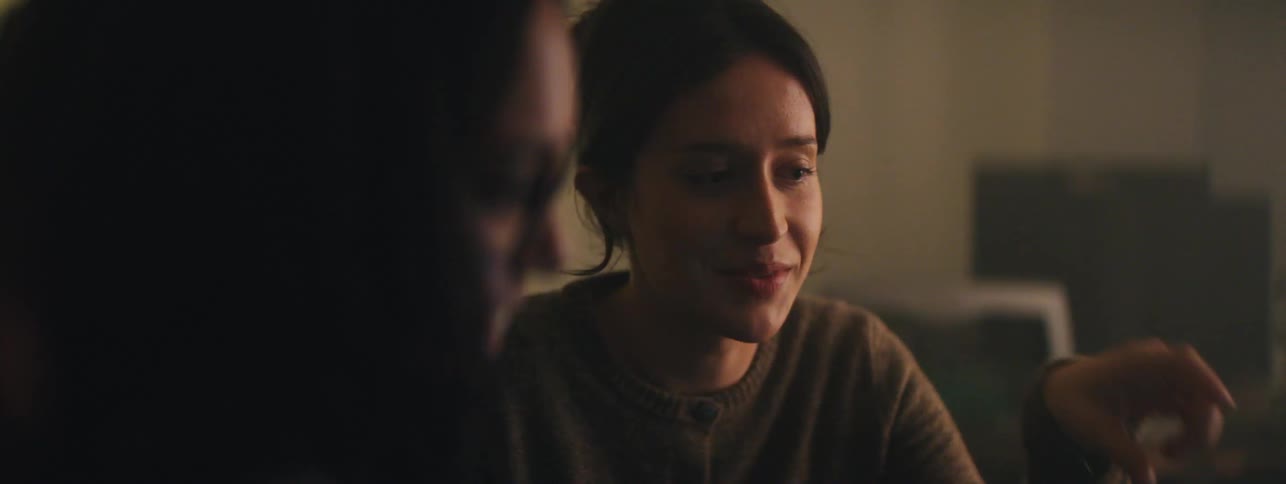 Two women sitting in a dimly lit room talking to each other