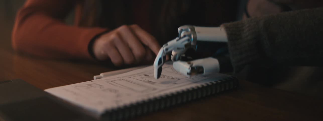 Students studying from a notebook with one using a robotic arm