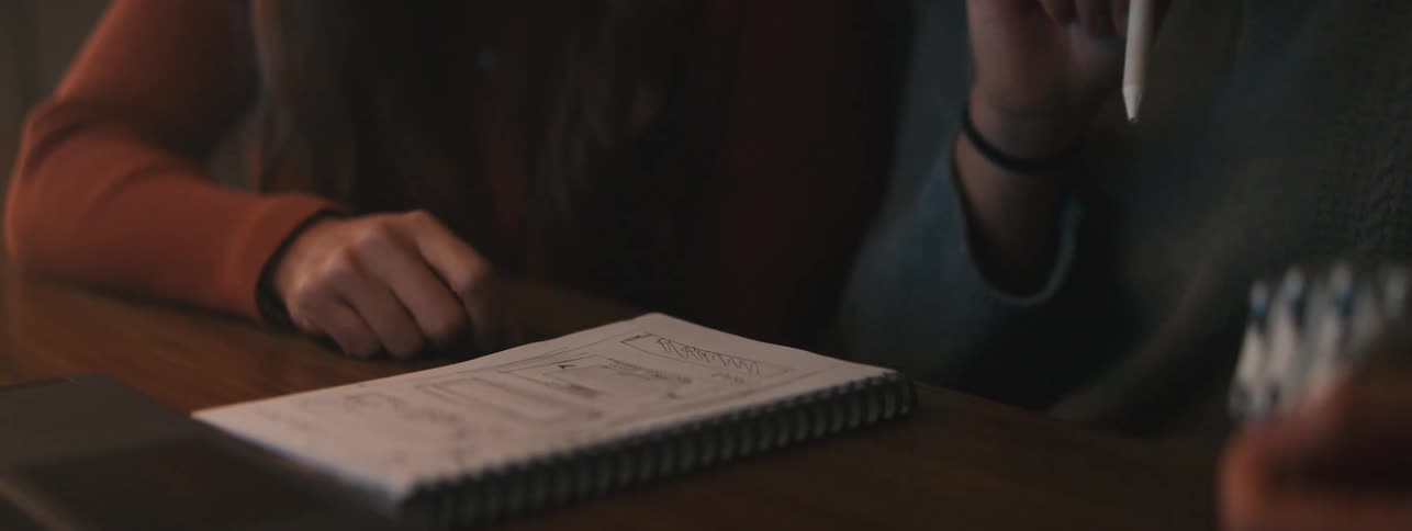 Three students sit at a table looking over a notebook with diagrams in them