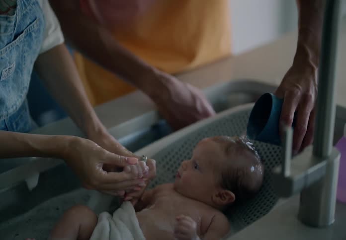 Pair of hands of a man and a woman bathing a baby