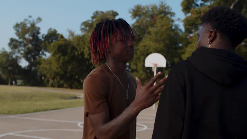 A young man helps a friend stand up from the ground of a basketball court