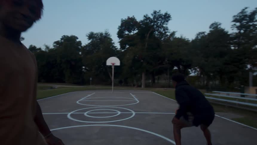 Two young men on an openair court playing basketball in the late afternoon