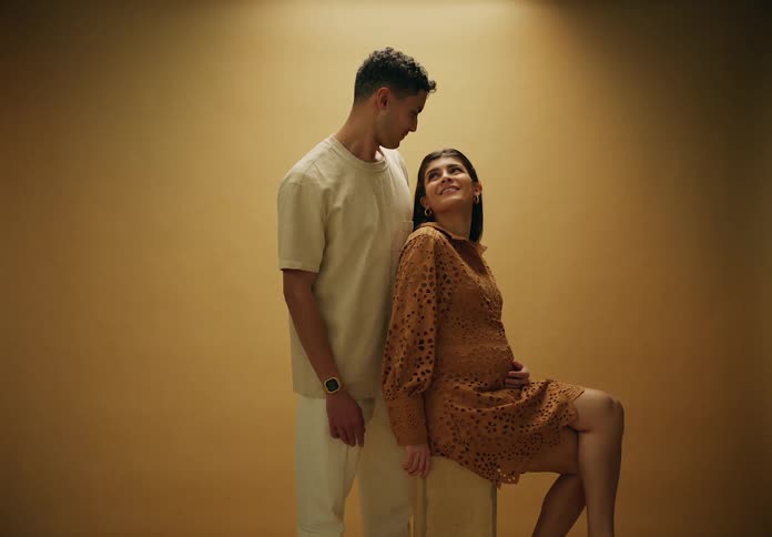 Pregnant woman sitting next to a man posing indoors