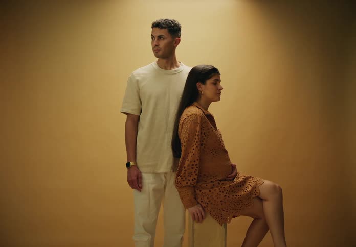 Man standing posing for photo next to his pregnant wife in a studio