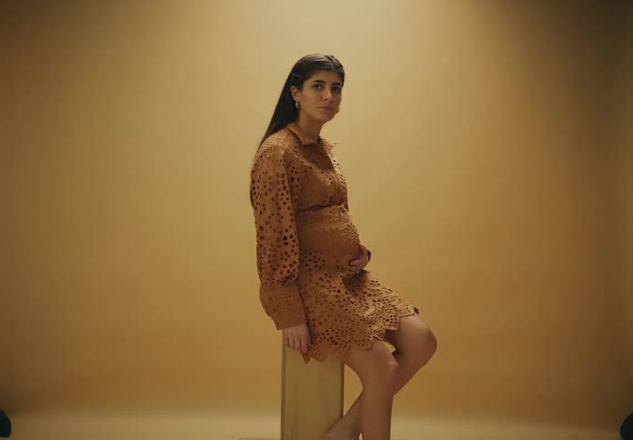 Expectant mother poses on a stool with a hand on her abdomen