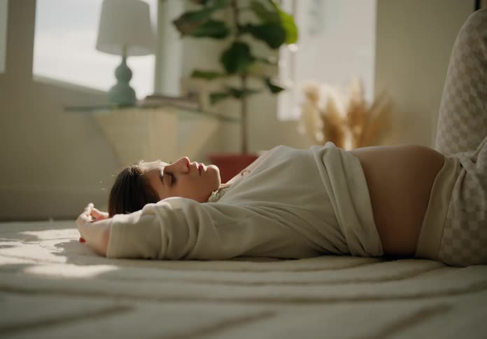 A pregnant woman lying on her back on a rug bathed in sunlight