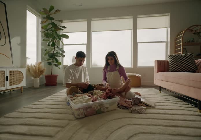 A man and a woman are sitting on the floor and looking through clothes that are in a large plastic container