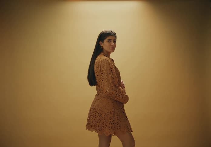 A woman stands with her back turned and then partially turns around and holds her pregnant belly and the background is orange colors