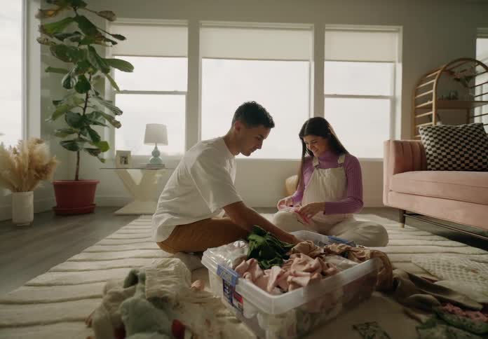 Man sitting next to his pregnant wife on a rug in the living room looking at baby clothes with her