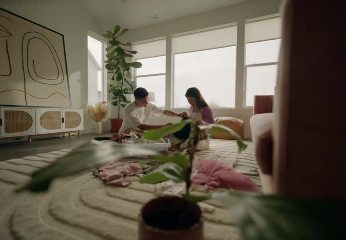 Couple sitting in living room on carpet looking at baby clothes