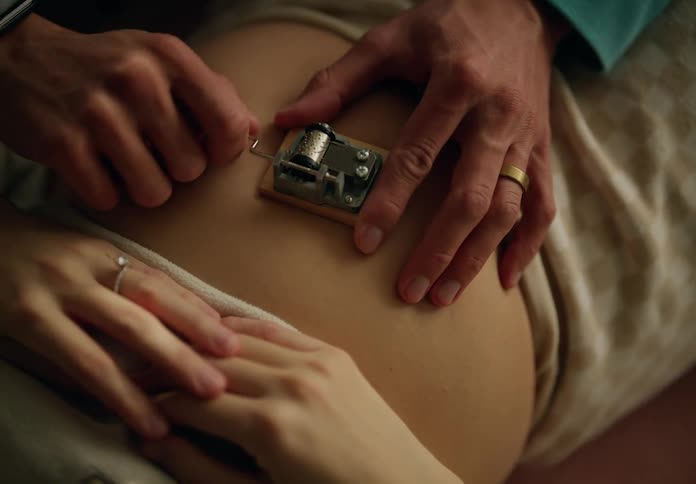 A hand playing a music box on a pregnant womans belly