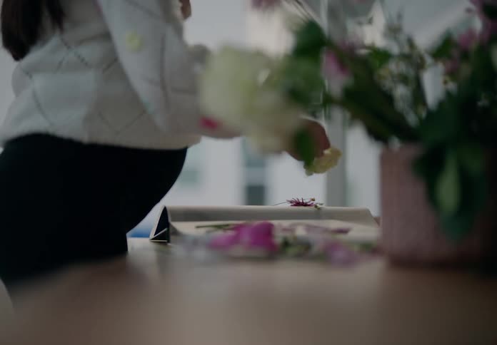 Pregnant woman picking flowers and putting them inside a book