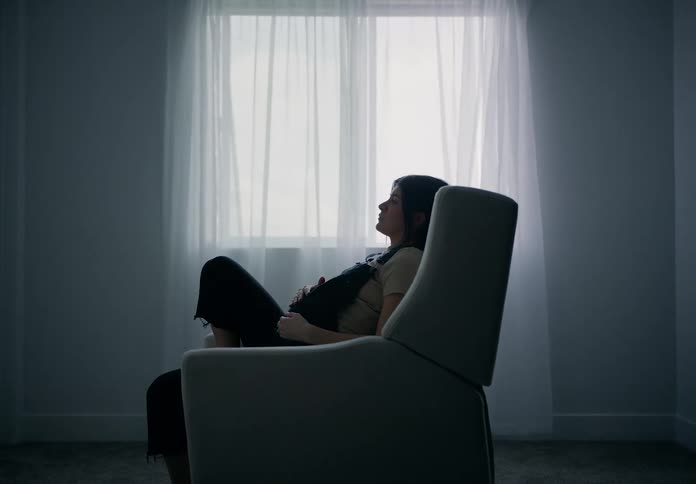 Pregnant woman sitting in an armchair next to a window with curtains