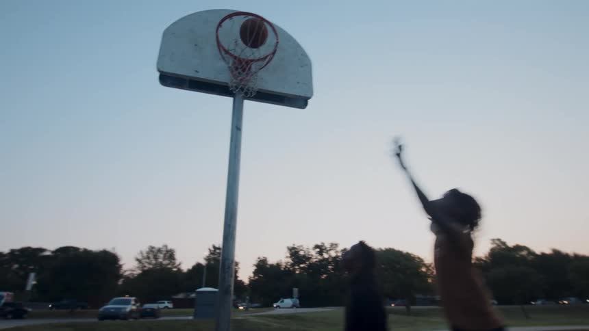 Boy jumping and scoring a point while playing basketball with his friend on a court