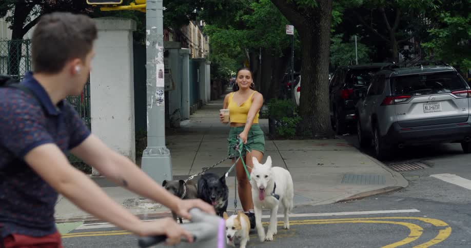A woman holding an iced coffee and crossing the street in the city with four dogs