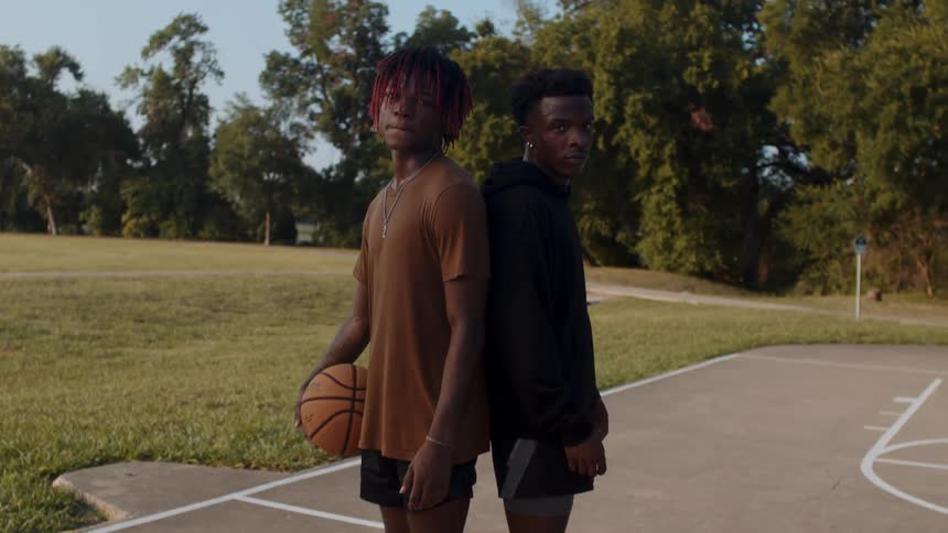 Two young men standing back to back on a court with one of them holding a basketball