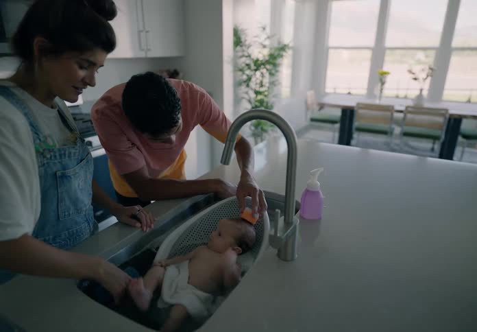 A young couple bathing a baby in the kitchen sink at home
