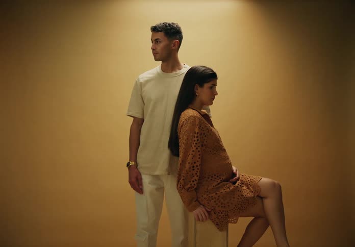 A pregnant couple stand together for a portrait against a beige background