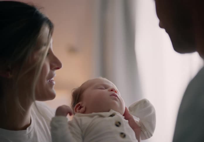 Father picking up baby and giving him a kiss together with mother and placing him in the crib
