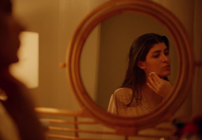 Woman sitting in front of a round mirror doing skin care