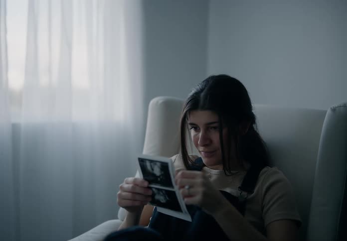 Expectant mother sitting at home smiles while looking at ultrasound pictures