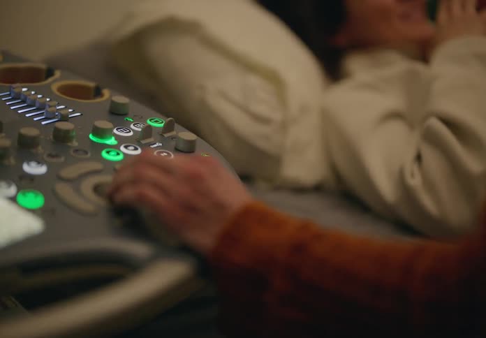 A doctors hand presses buttons on an ultrasound machine near a patient