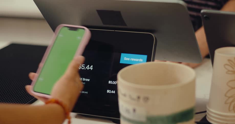 Person purchases coffee using their phone as a cashier looks on